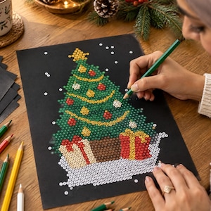 May include: A black sheet of paper featuring a dot-to-dot style Christmas tree illustration with green, red, and yellow circular patterns. The design includes a star topper and gift boxes at the base, with scattered white dots representing snow.