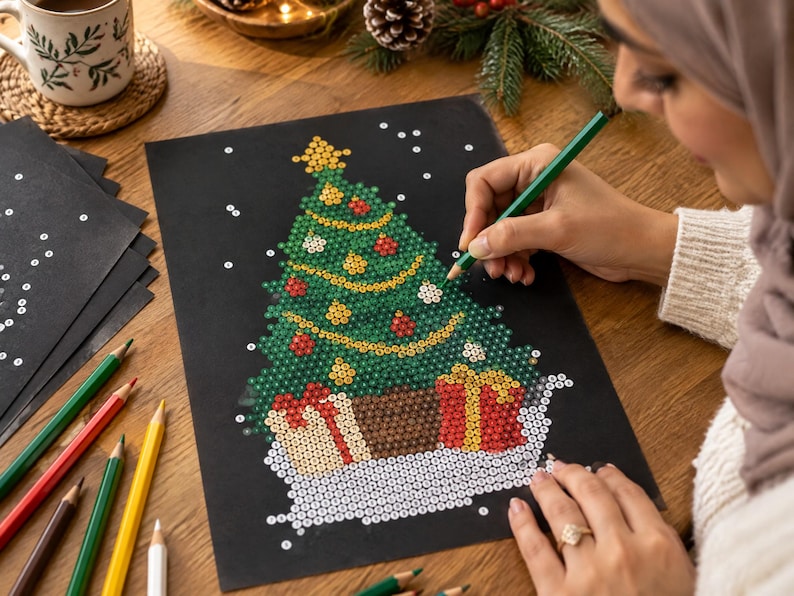 May include: A black sheet of paper featuring a dot-to-dot style Christmas tree illustration with green, red, and yellow circular patterns. The design includes a star topper and gift boxes at the base, with scattered white dots representing snow.
