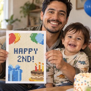 Puede incluir: Un proyecto de manualidades de pintura de diamantes rectangular con un diseño pixelado que muestra el texto HAPPY 2ND! en azul, rodeado de globos de colores, una caja de regalo azul y un pastel de cumpleaños con tres velas encendidas.