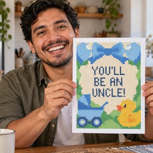 Peut inclure: Une impression rectangulaire pr&eacute;sentant un motif pix&eacute;lis&eacute; avec le texte "YOU'LL BE AN UNCLE!" en bleu fonc&eacute;. L'illustration comprend un grand n&oelig;ud bleu en haut, une poussette bleue &agrave; gauche et un canard en caoutchouc jaune &agrave; droite, le tout sur un fond vert avec une bulle centrale de couleur cr&egrave;me.