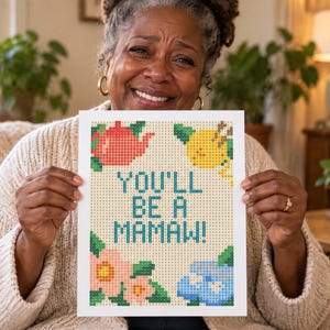 Op de afbeelding: Een rechthoekig diamond painting knutselproject met een lichtbeige achtergrond en een rasterpatroon. De tekst "YOU'LL BE A MAMAW!" is gedrukt in blauwgroen. Decoratieve elementen zijn onder meer een rode theepot, een gele citroen en roze en blauwe bloemen.