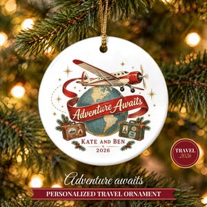May include: A round white ceramic ornament featuring a red and white airplane flying over a globe. A red ribbon banner reads Adventure Awaits. Below are two vintage suitcases, the text Kate and Ben, and the year 2026 with pine sprigs.
