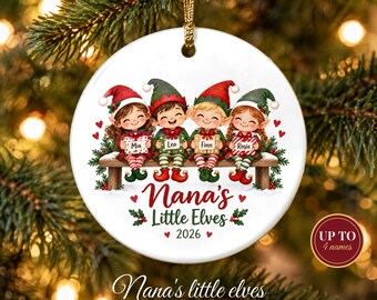 May include: A round white ceramic Christmas ornament featuring a colorful illustration of four children dressed as elves sitting on a wooden bench. Each elf holds a gift box labeled with the names Mia, Leo, Finn, and Rosie. The text reads Nana's Little Elves 2026.