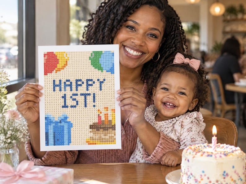 May include: A rectangular diamond painting craft project featuring a pixelated design with the text HAPPY 1ST! in blue, accompanied by colorful balloons, a blue gift box, and a birthday cake with three lit candles on a light tan background.