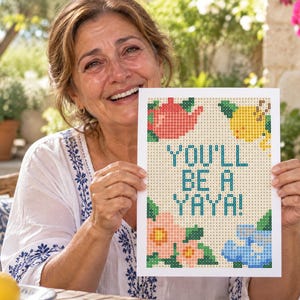 K&ouml;nnte beinhalten: Eine rechteckige wei&szlig;e Karte mit einem pixeligen Kreuzstich-Design und dem Text "YOU'LL BE A YAYA!" in Blau. Das Motiv zeigt eine rote Teekanne, eine gelbe Zitrone, eine rosa Blume und blaue Blumen, die alle in einem Rastermuster dargestellt sind.