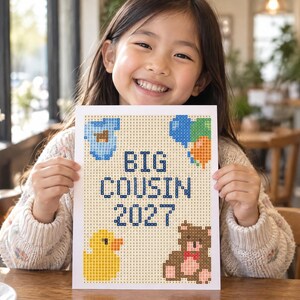 May include: A rectangular diamond painting canvas featuring the text BIG COUSIN 2027 in dark blue letters. The design includes a light blue baby onesie, a cluster of blue, green, and orange balloons, a yellow rubber duck, and a brown teddy bear.