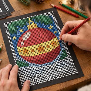 May include: A dot-to-dot coloring sheet on black paper featuring a red and yellow Christmas ornament design. The artwork is composed of a grid of white circles, some of which are filled in with red, yellow, green, and blue colored pencil.