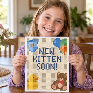 May include: A rectangular sign featuring a pixel art design with the text NEW KITTEN SOON! in dark blue. The design includes a blue cloud, a cluster of blue and orange balloons, a yellow rubber duck, and a brown teddy bear on a light background.
