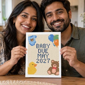 May include: A rectangular white sign featuring a pixelated cross-stitch design with the text BABY DUE MAY 2027 in dark blue. The design includes a blue baby onesie, a cluster of blue and orange balloons, a yellow rubber duck, and a brown teddy bear.