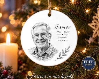 May include: A round white ceramic memorial ornament featuring a black and white sketch of a man wearing glasses and a collared shirt. The text reads James, 1950-2026, and Always in our hearts, accompanied by a small leaf illustration.