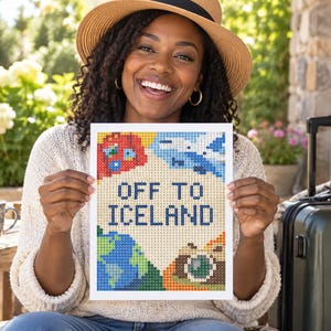 以下が含まれることがあります： OFF TO ICELANDという濃い青色の文字が中央に配置された、長方形のダイヤモンドペインティングのクラフト作品。明るいクリーム色の背景に、赤い飛行機、青い地球儀、カメラのカラフルなピクセルアート風のイラストが描かれています。