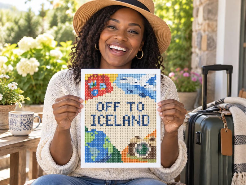 以下が含まれることがあります： OFF TO ICELANDという濃い青色の文字が中央に配置された、長方形のダイヤモンドペインティングのクラフト作品。明るいクリーム色の背景に、赤い飛行機、青い地球儀、カメラのカラフルなピクセルアート風のイラストが描かれています。