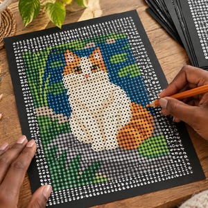 May include: A diamond painting kit featuring a cat with white and orange fur sitting among green foliage. The black canvas is printed with a grid of symbols for colour-coded placement. A stack of additional black canvases sits nearby.