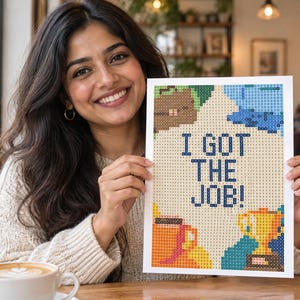 May include: A rectangular diamond painting craft project featuring a grid pattern with the text I GOT THE JOB! in dark blue. The design includes colorful pixelated illustrations of a brown briefcase, a gold trophy, and a coffee mug on a light background.