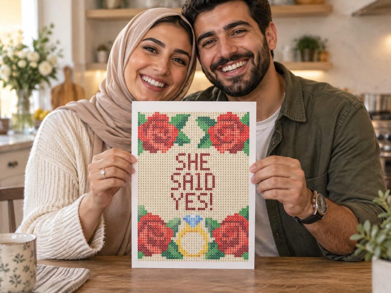 May include: A rectangular print featuring a cross-stitch style design with the text "SHE SAID YES!" in red letters. The design includes four red roses with green leaves in the corners and a yellow engagement ring with a blue diamond at the bottom.