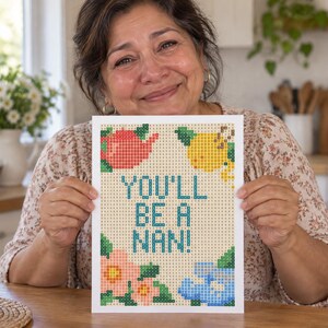 Puede incluir: Un proyecto de manualidades de pintura de diamantes rectangular con un patrón de cuadrícula y el texto "YOU'LL BE A NAN!" en azul. El diseño incluye una tetera roja, un limón amarillo, flores rosas y flores azules, formadas por cuadrados.