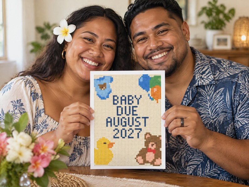 May include: A rectangular white sign featuring a pixelated cross-stitch design with the text BABY DUE AUGUST 2027 in dark blue. The design includes a blue baby onesie, a cluster of blue, green, and orange balloons, a yellow duck, and a brown teddy bear.