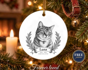 May include: A round white ceramic memorial ornament featuring a black and white sketch of a cat. Below the cat is a banner with the text Luna, 2010-2026, and Forever Loved. The ornament is suspended by a gold cord and framed by laurel leaves.