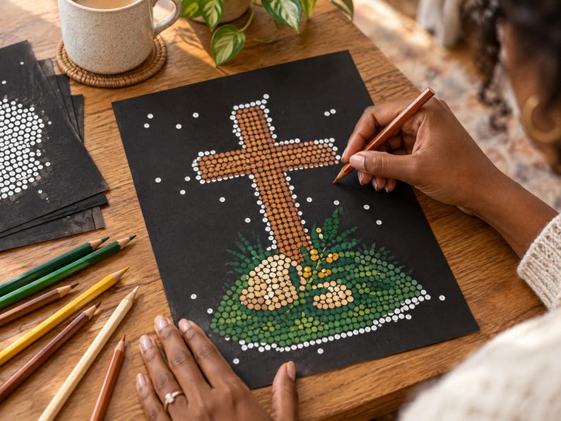 K&ouml;nnte beinhalten: Ein schwarzes Blatt Papier mit einer Punkt-Illustration eines braunen Kreuzes, umgeben von gr&uuml;nem Blattwerk und kleinen wei&szlig;en Punkten. Das Kunstwerk ist in Pointillismus-Technik erstellt und mehrere Buntstifte liegen auf dem Tisch bereit.