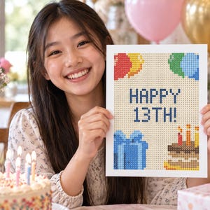 May include: A rectangular white print featuring a pixelated design with the text HAPPY 13TH! in dark blue. The graphic includes colorful balloons in red, yellow, green, and blue, a blue gift box, and a brown birthday cake with three lit candles.