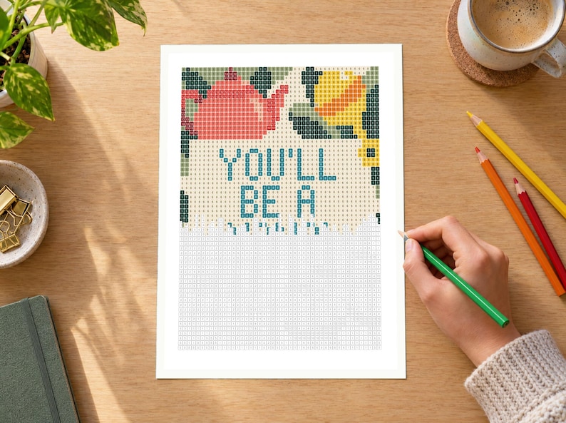 May include: A cross-stitch pattern printed on white paper featuring a red teapot, a yellow lemon, and green leaves at the top. The text "YOU'LL BE A" is printed in blue block letters in the center, with a grid of empty squares below.