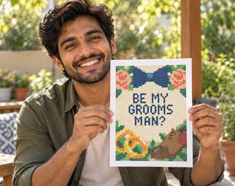 May include: A rectangular print featuring a cross-stitch style design with the text BE MY GROOMSMAN? in dark blue. The design includes a blue bow tie, two pink roses, two gold rings, and a brown dress shoe, all set against a white background.