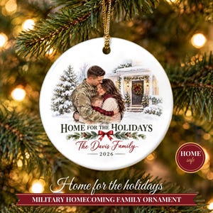 Peut inclure: Une décoration de Noël ronde en céramique blanche avec une illustration imprimée d'une famille s'étreignant devant une maison. Le texte indique HOME FOR THE HOLIDAYS, The Davis Family et 2026. Elle est suspendue par un cordon doré.
