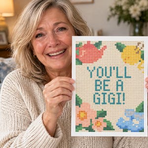 May include: A rectangular diamond painting canvas featuring a grid pattern with the text YOU'LL BE A GIGI! in blue. The design includes a pink teapot, a yellow lemon, a pink flower, and a blue baby onesie, all rendered in a pixelated style.