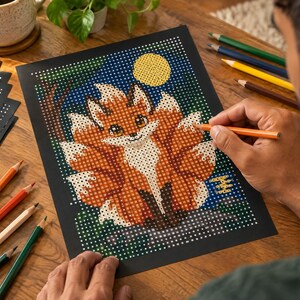 K&ouml;nnte beinhalten: Ein Punkt-zu-Punkt-Malblatt auf schwarzem Papier mit einer Illustration eines Fuchses mit mehreren Schw&auml;nzen in Orange, Wei&szlig; und Braun. Das Design zeigt einen gelben Mond vor einem dunkelblauen Hintergrund, ausgef&uuml;llt mit Buntstiften.