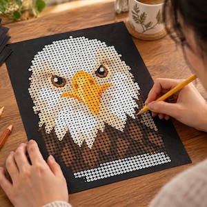May include: A paint-by-number kit featuring a bald eagle portrait on black paper. The eagle has a white head, a bright yellow beak, and brown feathers. The design is composed of small numbered circles to be filled with color using the provided pencils.