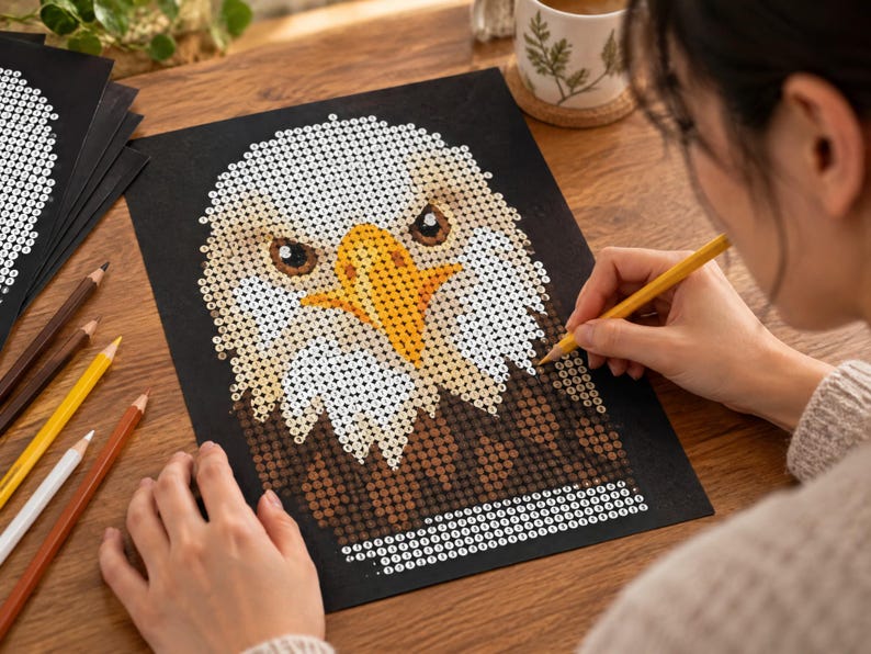 May include: A paint-by-number kit featuring a bald eagle portrait on black paper. The eagle has a white head, a bright yellow beak, and brown feathers. The design is composed of small numbered circles to be filled with color using the provided pencils.