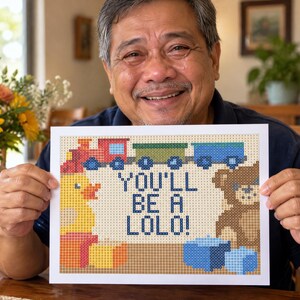 Op de afbeelding: Een rechthoekig bord met een gepixeld ontwerp met een trein, een gele eend, een bruine teddybeer en blauwe blokken. De tekst in het midden luidt "YOU'LL BE A LOLO!". Het ontwerp maakt gebruik van een rasterpatroon met diverse kleuren zoals rood, groen, blauw, geel en bruin.