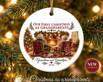 May include: A round white ceramic ornament featuring the text Our First Christmas As Grandparents and Grandma and Grandpa 2026. The illustration shows two people in rocking chairs by a fireplace with a cat, a tree, and stockings.