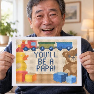 May include: A rectangular print featuring a pixelated design with the text YOU'LL BE A PAPA! in blue. The image includes a red and green train, a yellow rubber duck, a brown teddy bear, and blue blocks, all rendered in a grid-like pattern.