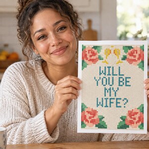 Puede incluir: Un proyecto de manualidades de pintura de diamantes rectangular con el texto WILL YOU BE MY WIFE? en letras azules. El dise&ntilde;o est&aacute; enmarcado por cuatro grupos de rosas rosadas con hojas verdes y dos peque&ntilde;as copas de champ&aacute;n amarillas arriba.