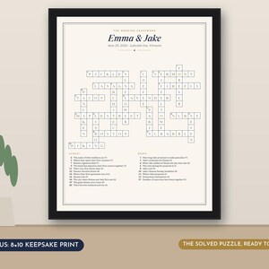May include: A framed wedding crossword puzzle print titled Emma & Jake, dated June 20, 2026, in Lakeside Inn, Vermont. The white print features black text and grid lines, with numbered clues listed below the puzzle. The frame is black with a thin border.
