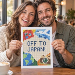 Puede incluir: Un proyecto de manualidades de diamond painting rectangular con un diseño pixelado y el texto OFF TO JAPAN! en azul. La obra incluye iconos coloridos de un globo terráqueo rojo, un avión azul, una tierra verde y azul, y una cámara marrón sobre fondo crema.