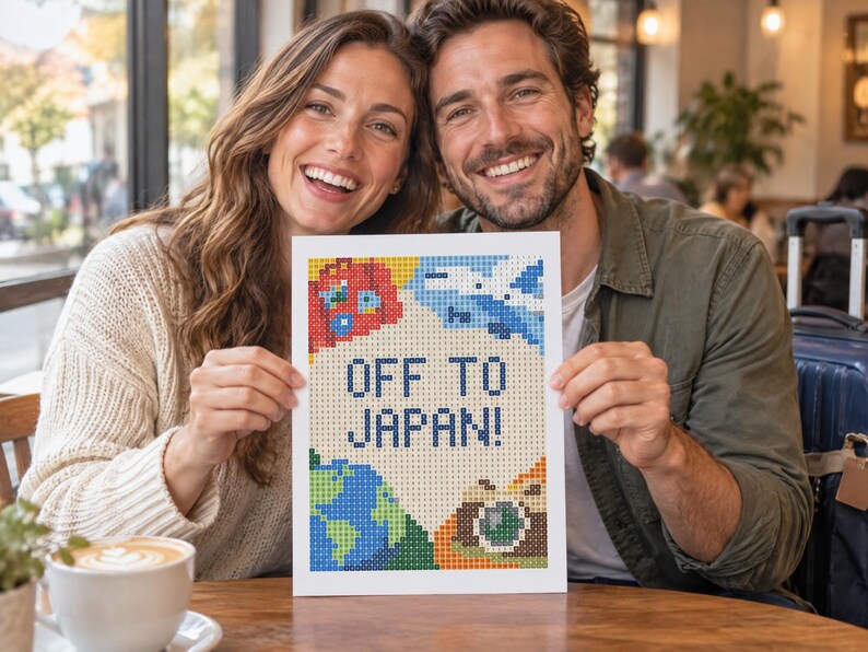 May include: A rectangular diamond painting craft project featuring a pixelated design with the text OFF TO JAPAN! in blue. The artwork includes colorful icons of a red globe, a blue airplane, a green and blue earth, and a brown camera on a cream background.