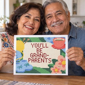 Puede incluir: Un letrero rectangular con un diseño de punto de cruz pixelado con el texto YOU'LL BE GRANDPARENTS en letras rojo oscuro. La ilustración incluye un ovillo de lana amarillo, patucos azules, una taza roja y flores rosas sobre un fondo verde.