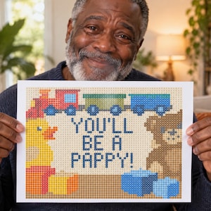 K&ouml;nnte beinhalten: Ein rechteckiger Druck mit einem verpixelten Design und dem Text YOU'LL BE A PAPPY! in Dunkelblau. Das Bild zeigt einen rot-blauen Zug, eine gelbe Quietscheente, einen braunen Teddyb&auml;ren und blaue Bl&ouml;cke, alles in einem gitterartigen Muster.