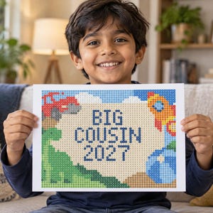May include: A rectangular craft project featuring a pixelated design with the text BIG COUSIN 2027 in dark blue. The image includes a green dinosaur, a red vehicle, a rocket ship, and a blue planet against a light tan and blue background.