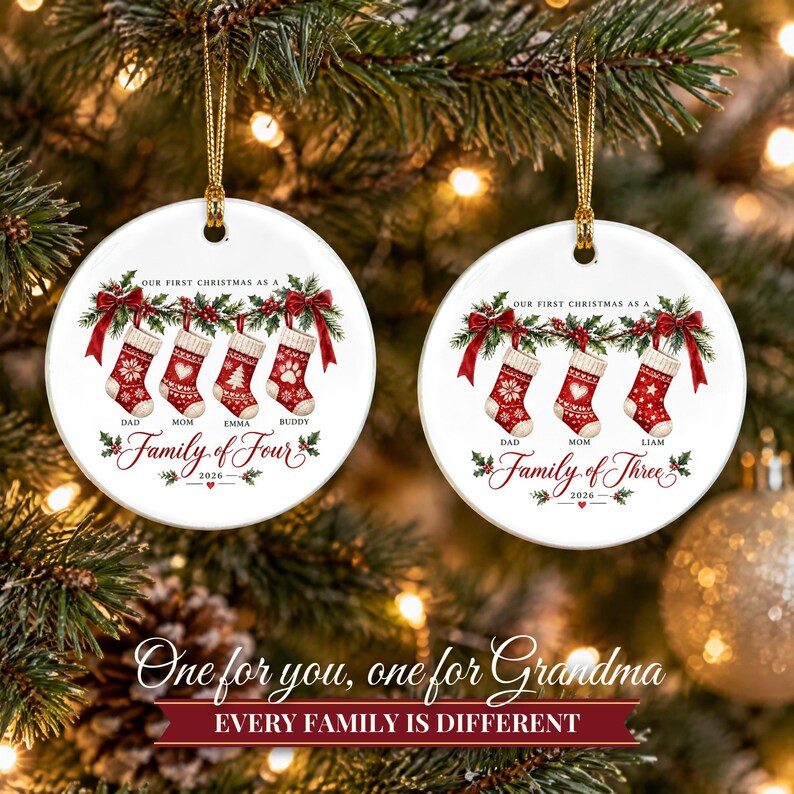 May include: Two round white ceramic ornaments with gold hanging strings. The left ornament features four red stockings with names Dad, Mom, Emma, Buddy and text Our First Christmas as a Family of Four 2026. The right shows three stockings with names Dad, Mom, Liam and text Our First Christmas as a Family of Three 2026.