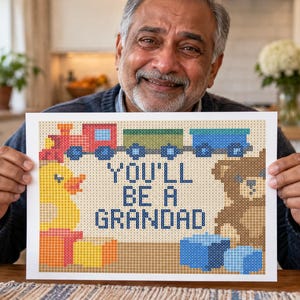 Puede incluir: Una impresi&oacute;n rectangular con un dise&ntilde;o de estilo punto de cruz pixelado que muestra un tren de juguete, un patito de goma amarillo y un oso de peluche marr&oacute;n. El texto central dice "YOU'LL BE A GRANDAD" en letras azules, rodeado de bloques.
