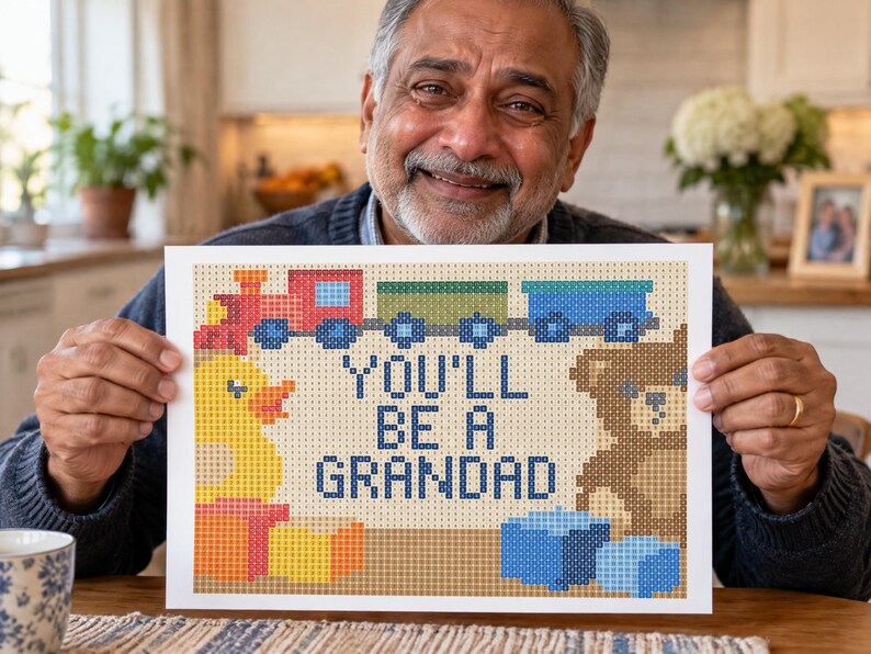 Puede incluir: Una impresi&oacute;n rectangular con un dise&ntilde;o de estilo punto de cruz pixelado que muestra un tren de juguete, un patito de goma amarillo y un oso de peluche marr&oacute;n. El texto central dice "YOU'LL BE A GRANDAD" en letras azules, rodeado de bloques.
