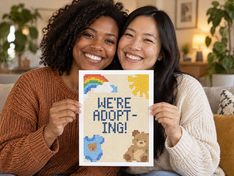 May include: A rectangular sign featuring a pixelated design with the text WE'RE ADOPTING! in dark blue. The design includes a colorful rainbow, a yellow sun, a light blue baby onesie, and a brown teddy bear on a light beige grid background.