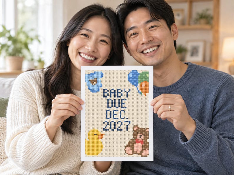 May include: A rectangular white sign featuring a pixelated cross-stitch design with the text "BABY DUE DEC. 2027" in dark blue. The design includes a blue baby onesie, colourful balloons, a yellow rubber duck, and a brown teddy bear with a red bow.