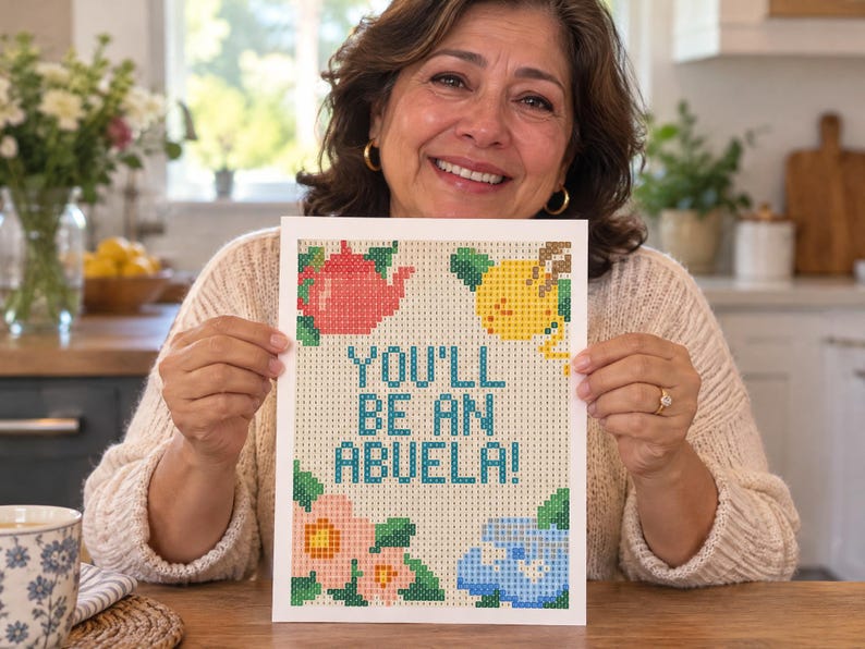 May include: A rectangular craft project featuring a grid pattern with the text YOU'LL BE AN ABUELA! in blue. The design includes a red teapot, a yellow lemon, and pink and blue flowers, all composed of small square tiles on a light background.