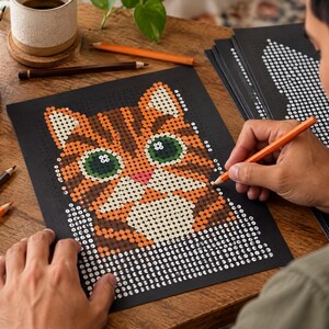 以下が含まれることがあります： 黒い背景にオレンジ色のトラ猫のイラストが描かれた、数字で色を塗るアクティビティシート。猫は大きな緑色の目とピンクの鼻をしており、色鉛筆で塗りつぶすのを待っている番号付きの円が並んでいます。