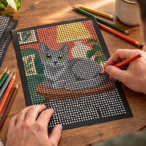 May include: A color-by-number activity sheet featuring a gray cat with green eyes sitting indoors. The image is composed of small numbered circles on a black background, with a partially colored section showing the cat, a lamp, and foliage.