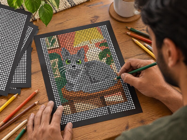 May include: A dot-to-dot coloring sheet featuring a gray cat sitting on a surface, rendered in a grid of numbered circles. The image includes a yellow lamp, green foliage, and a brown table, with several colored pencils scattered nearby.